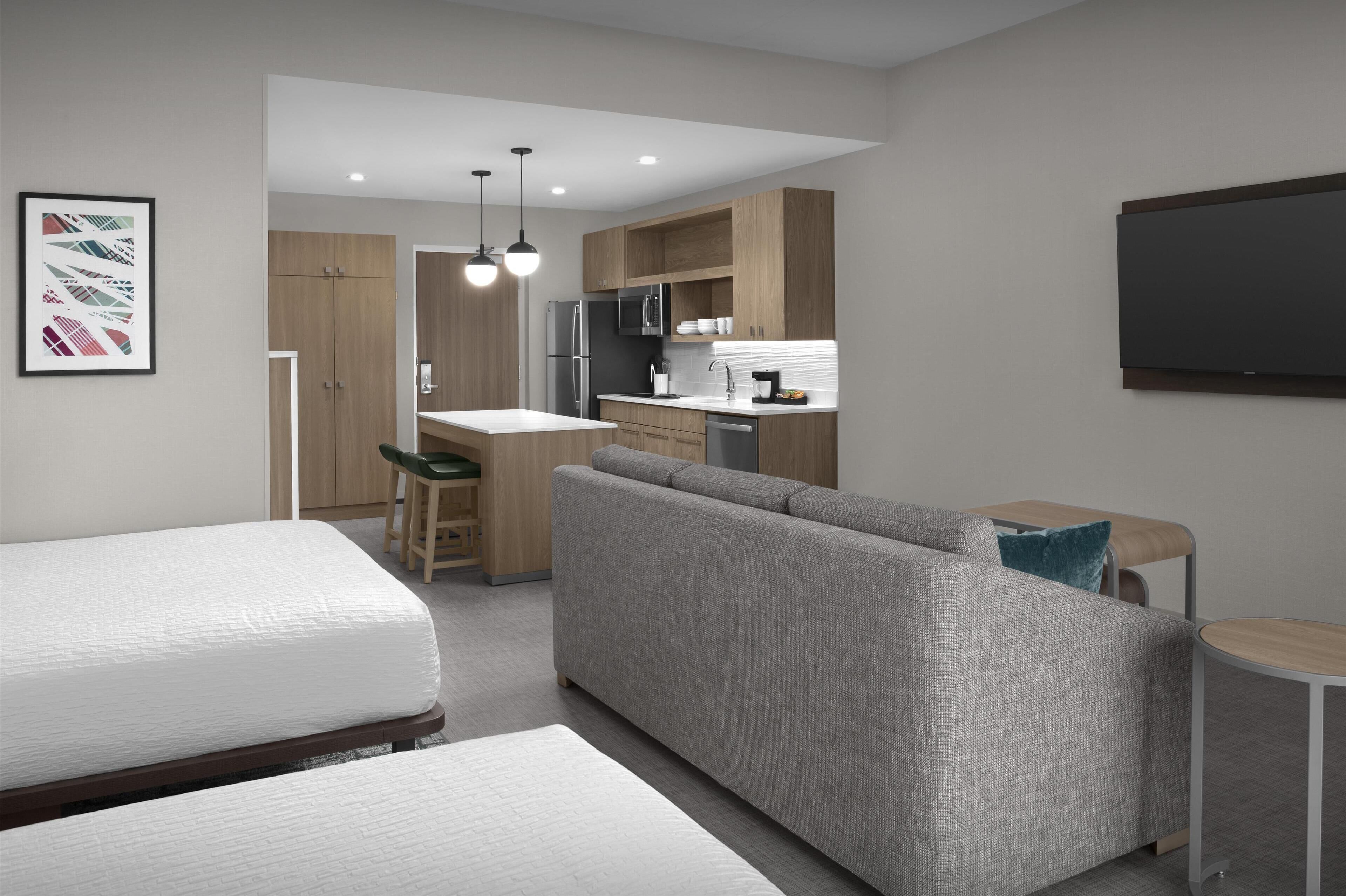 A modern, compact living space with a kitchenette, a sofa, a dining area, and a bed.