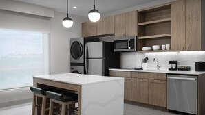 A modern kitchen with a central island, wooden cabinets, a built-in washer and dryer, and a view of the city. - Homewood Suites By Hilton Columbia Downtown (Columbia)