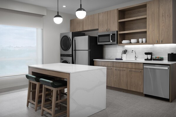 A modern kitchen with a central island, wooden cabinets, a built-in washer and dryer, and a view of the city.