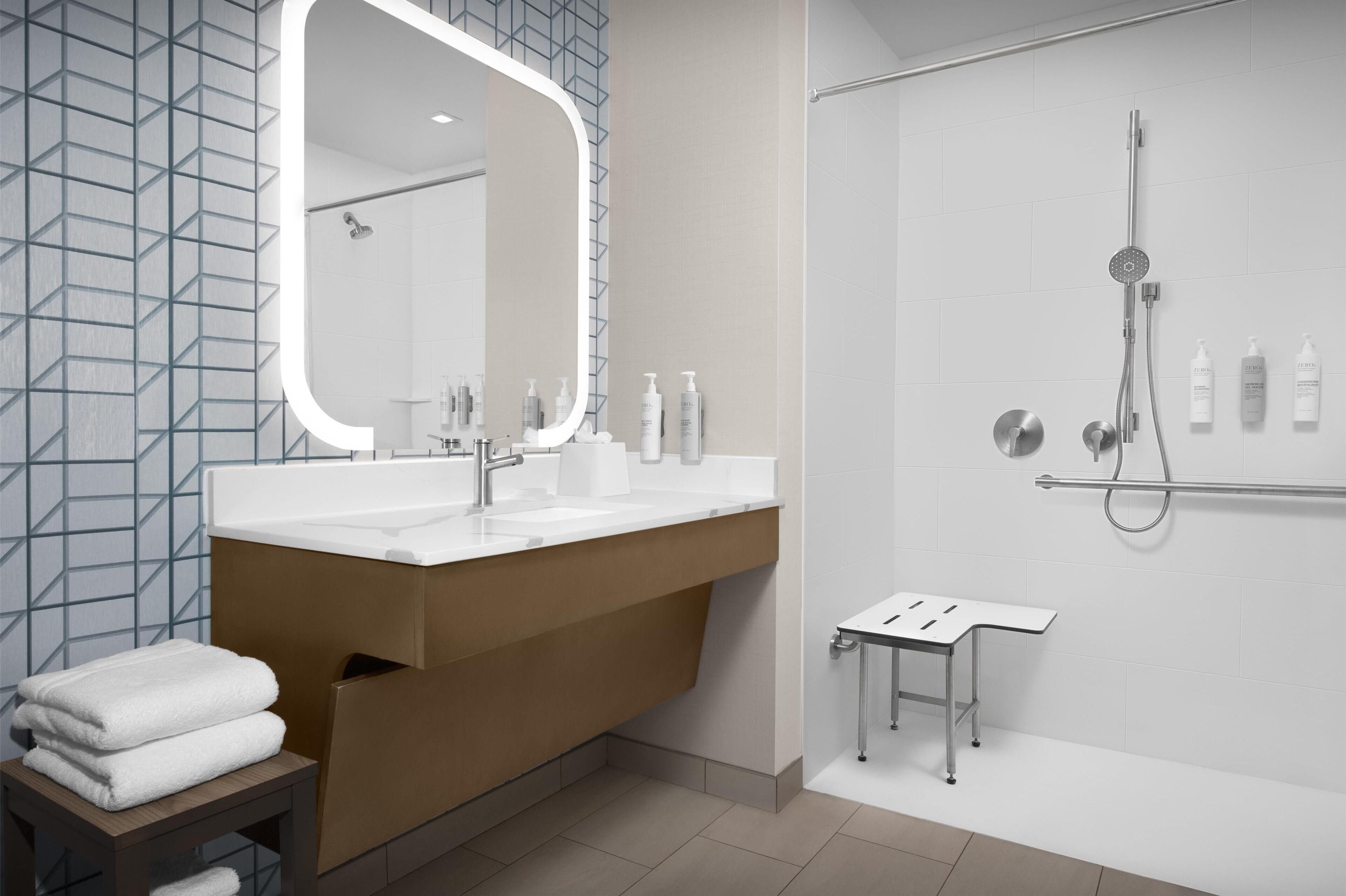 A modern bathroom with a large mirror, a shower, and a vanity with toiletries.