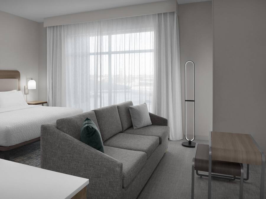 A modern hotel room with a bed, a grey sofa, a small table, and a floor lamp.