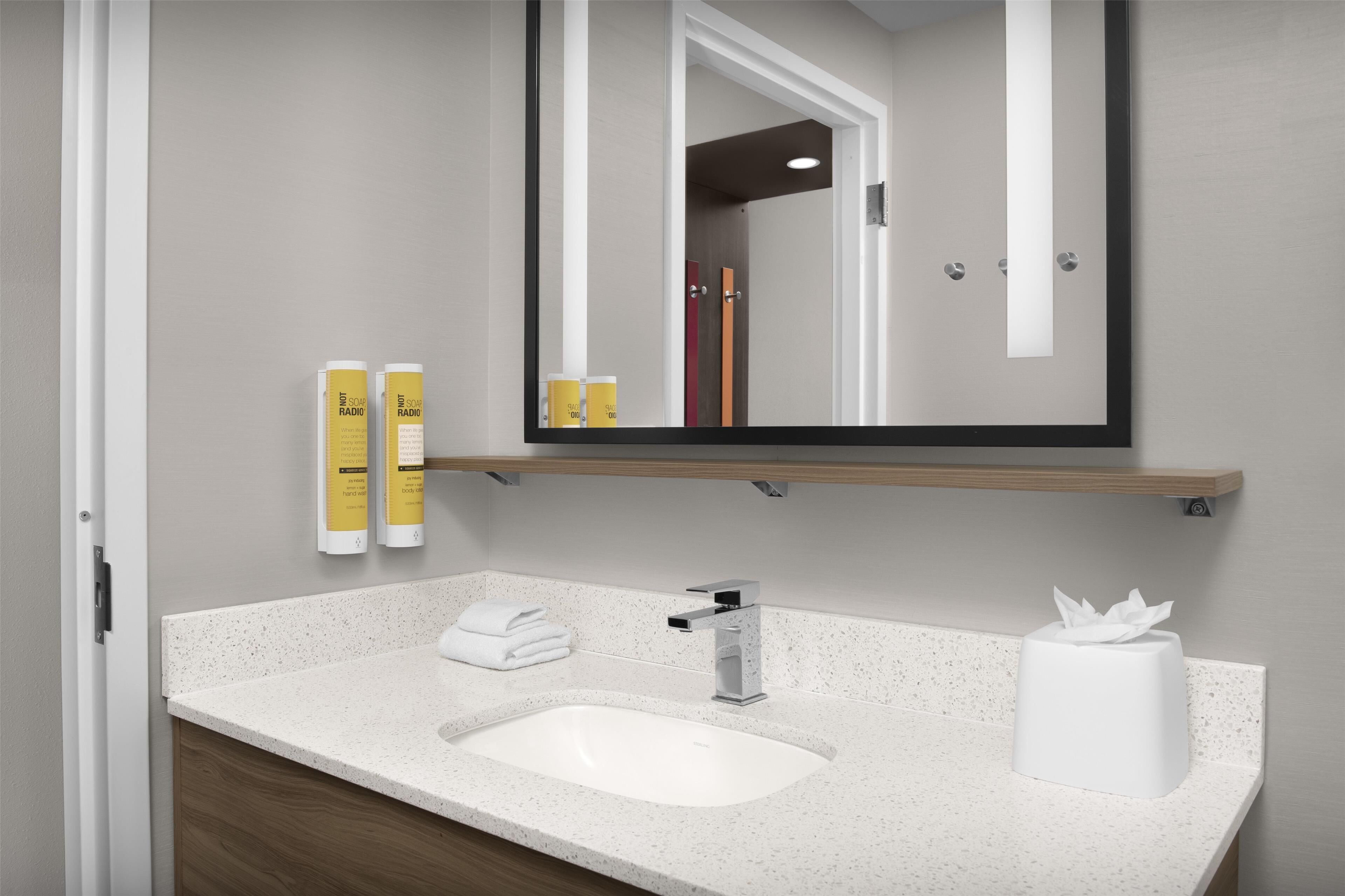 A bathroom with a white sink, a mirror, and two yellow bottles on a shelf.