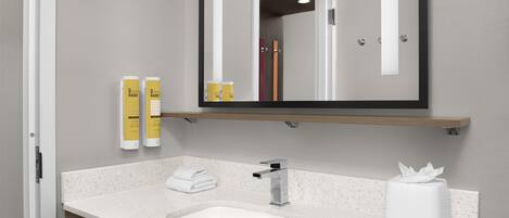 A bathroom with a white sink, a mirror, and two yellow bottles on a shelf.