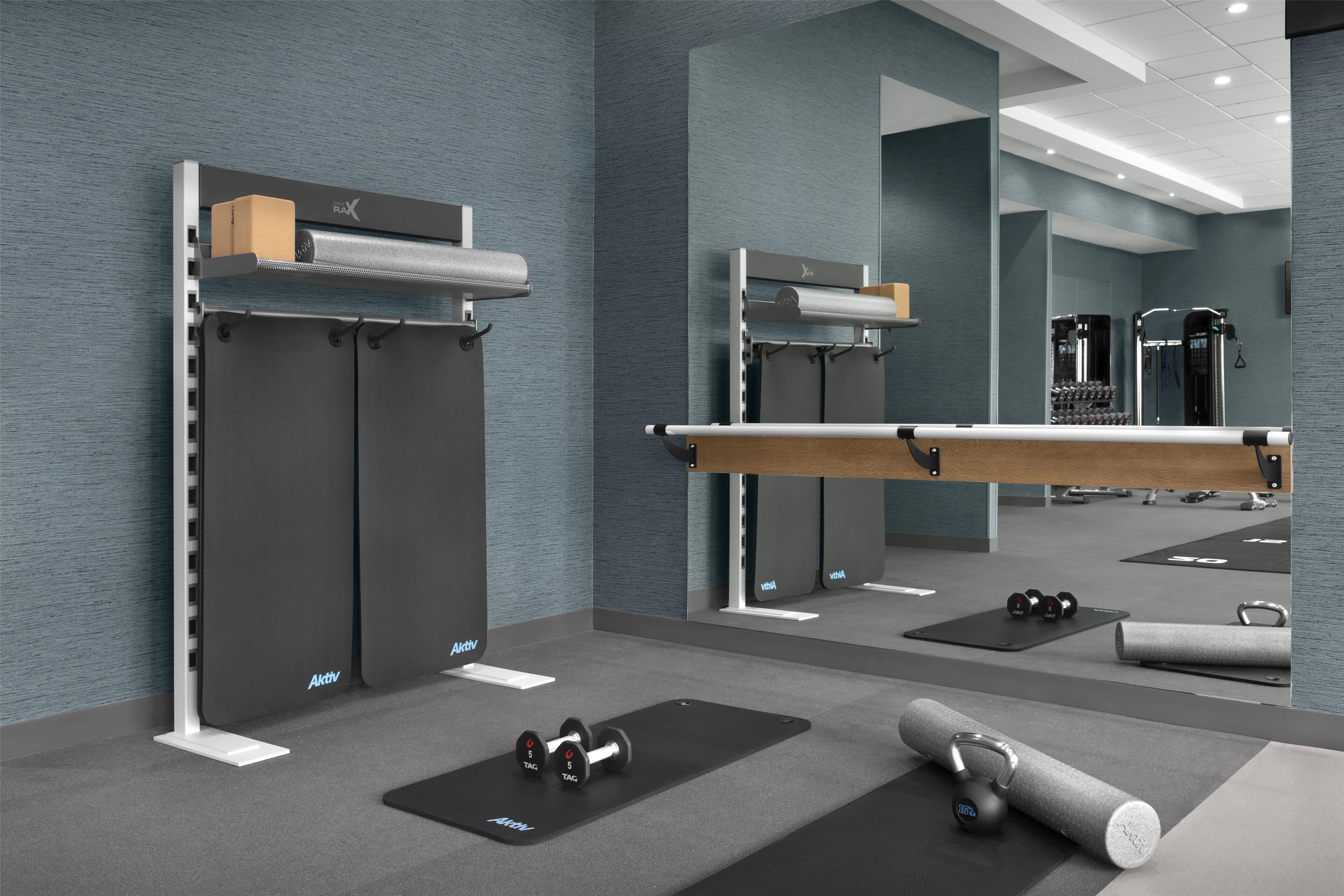 A modern gym with weightlifting equipment, exercise mats, and a mirrored wall.