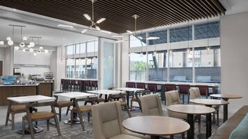 Un espace de restauration moderne, avec des tables et des chaises, de grandes fenêtres et une cuisine en arrière-plan.
