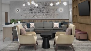 A modern lounge area with a sectional sofa, two armchairs, a coffee table, and a wall-mounted TV. - Tru By Hilton Columbia Downtown (Columbia)
