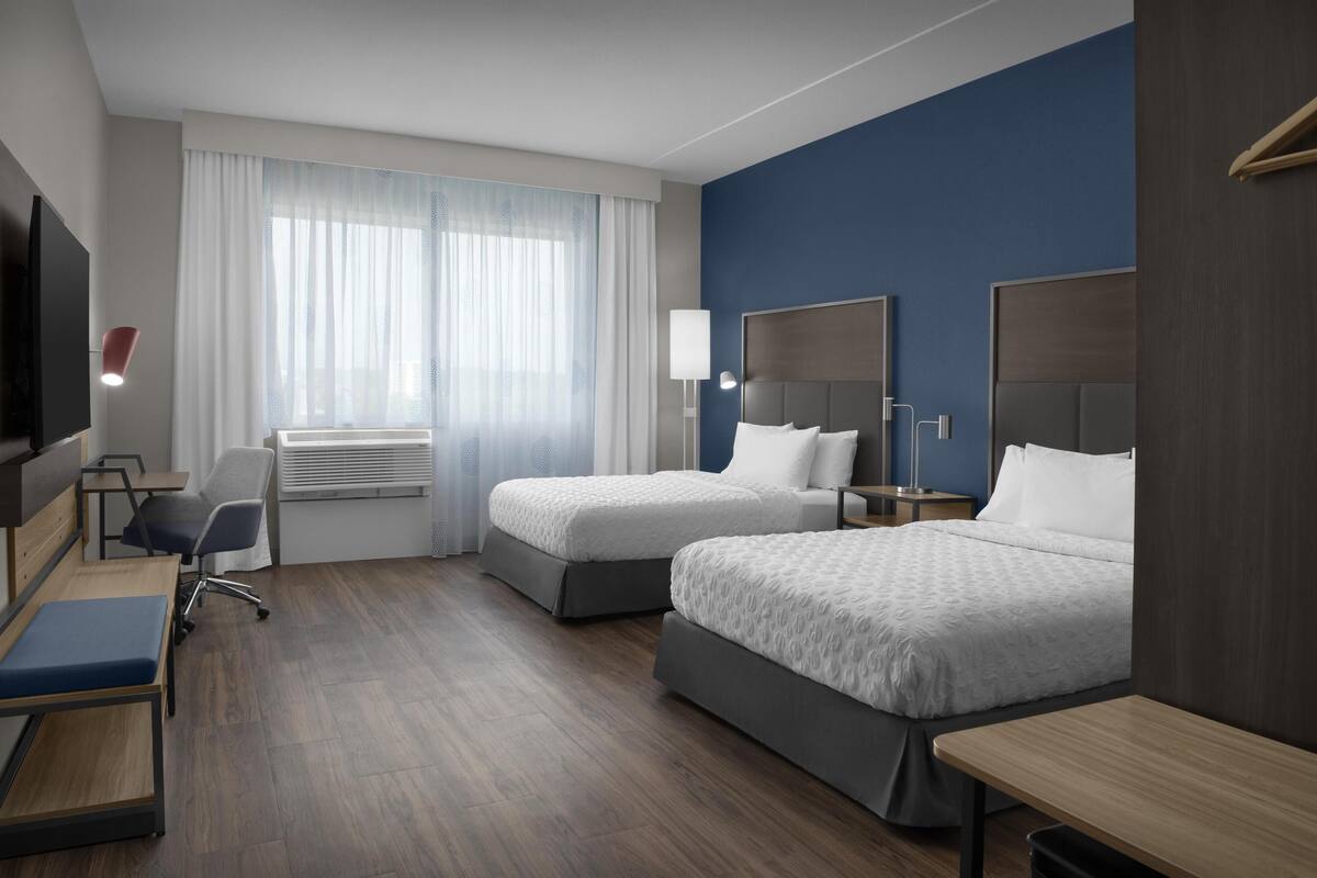 Una habitación de hotel con dos camas, un escritorio, una silla, un televisor y una ventana con cortinas.