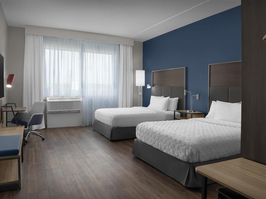 A hotel room with two beds, a desk, a chair, a TV, and a window with curtains.