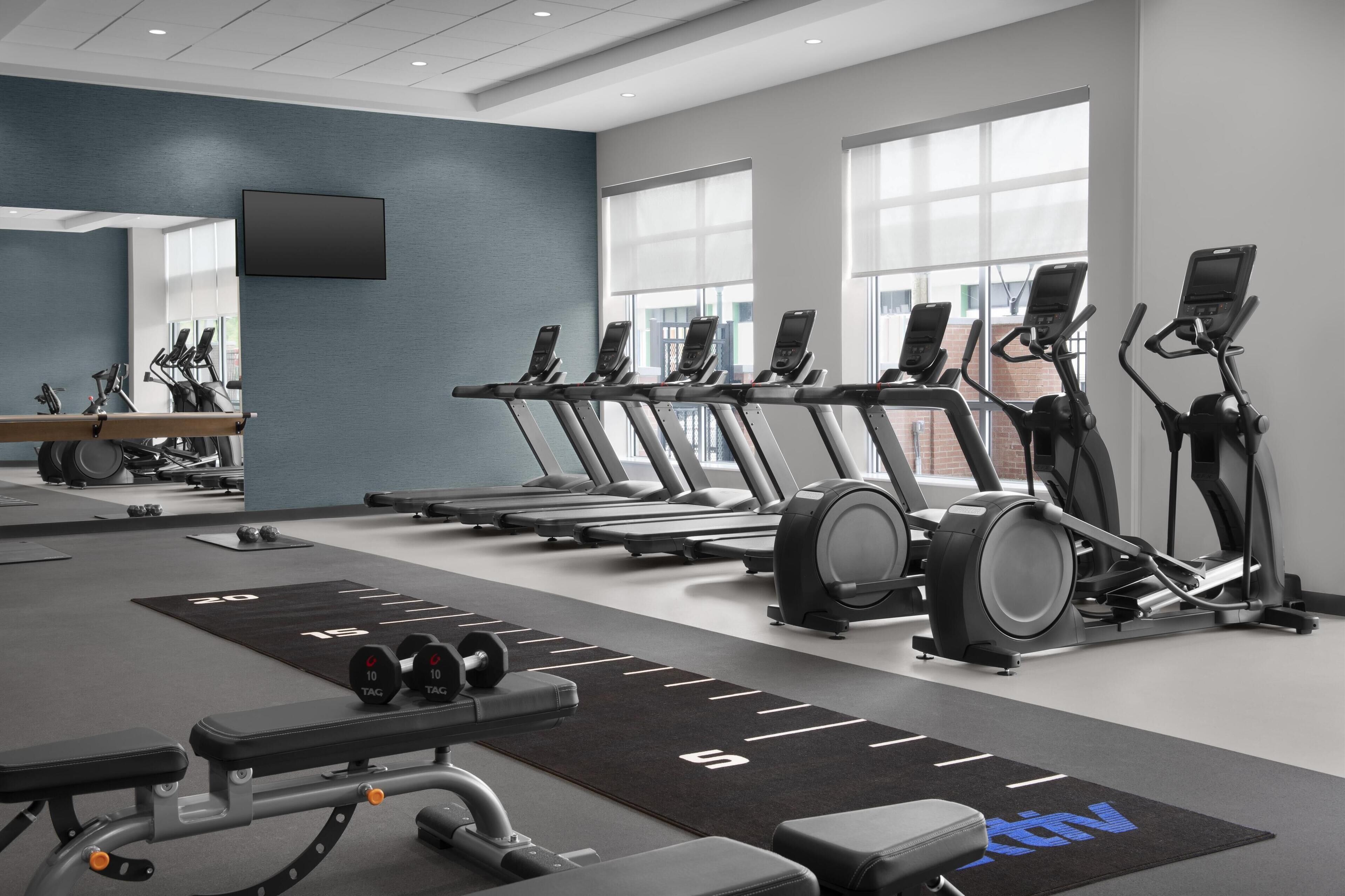A modern gym with treadmills, elliptical machines, and weightlifting equipment.