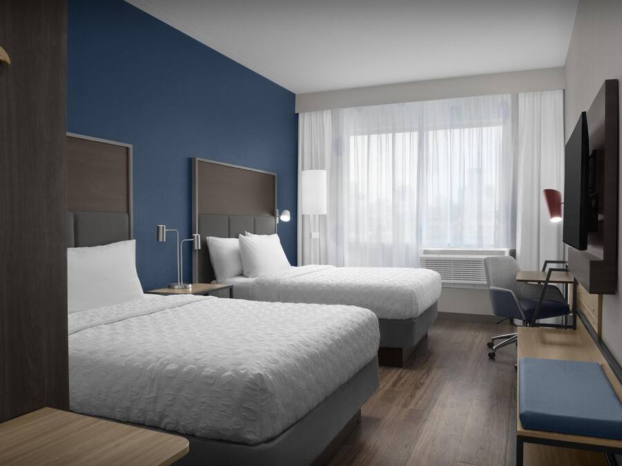 A hotel room with two beds, a desk, a chair, a TV, and a window with curtains.