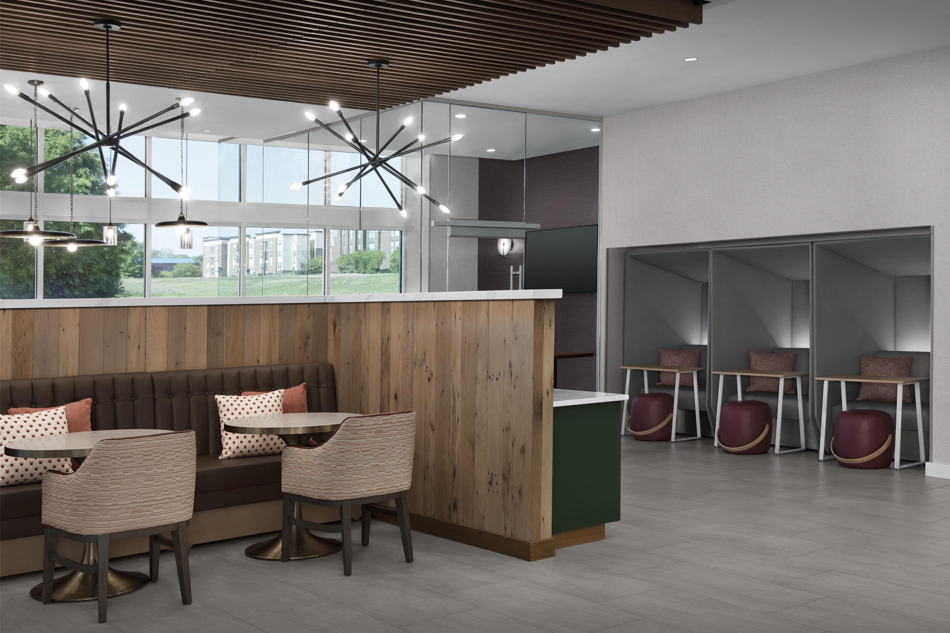 A modern interior with a wooden accent wall, a seating area with tables and chairs, and a kitchen area with a large window.