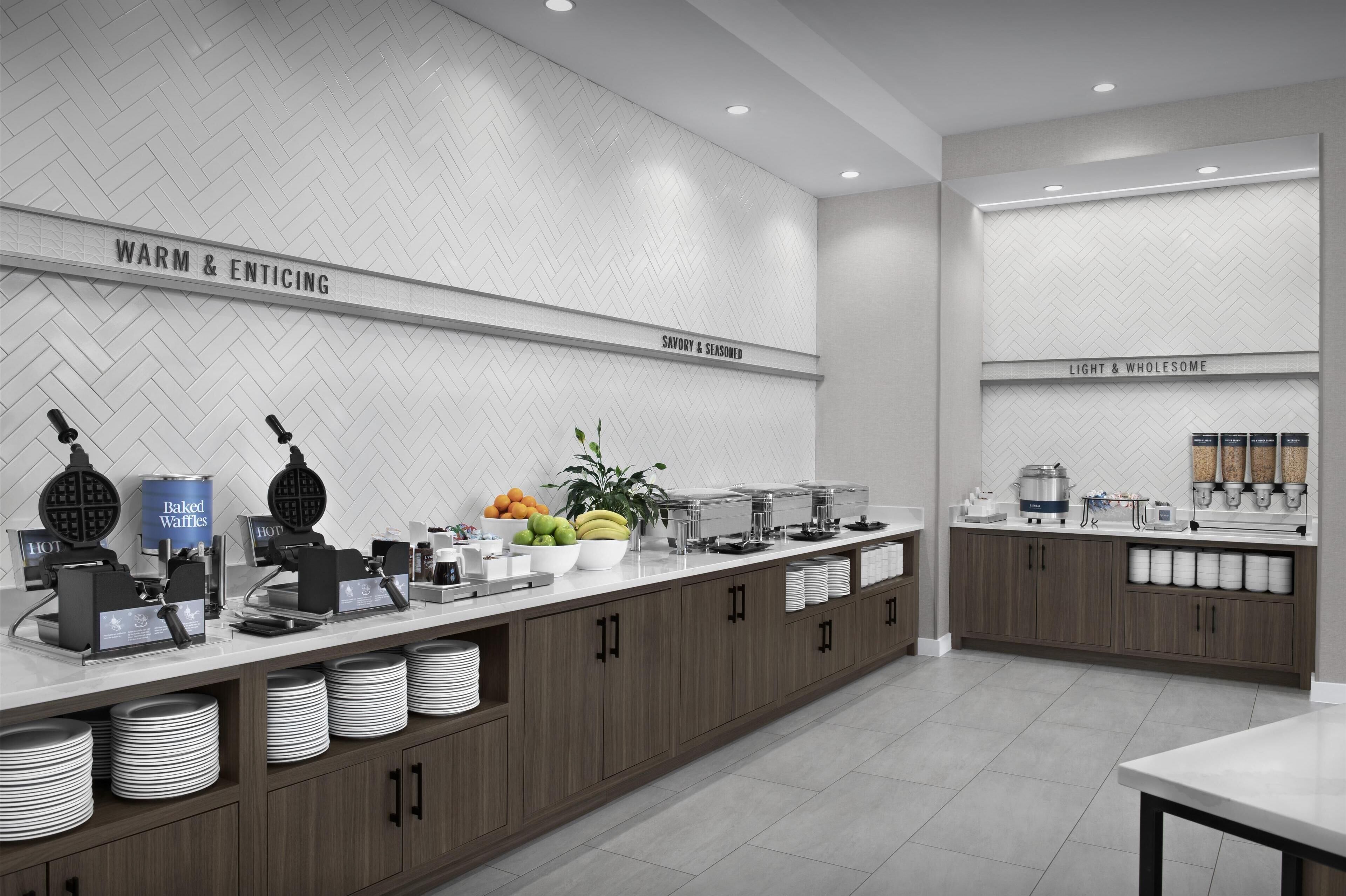 A modern kitchen with a herringbone-patterned backsplash, labeled sections for different food categories, and a variety of appliances and food items.