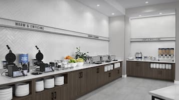 A modern kitchen with a herringbone-patterned backsplash, labeled sections for different food categories, and a variety of appliances and food items.