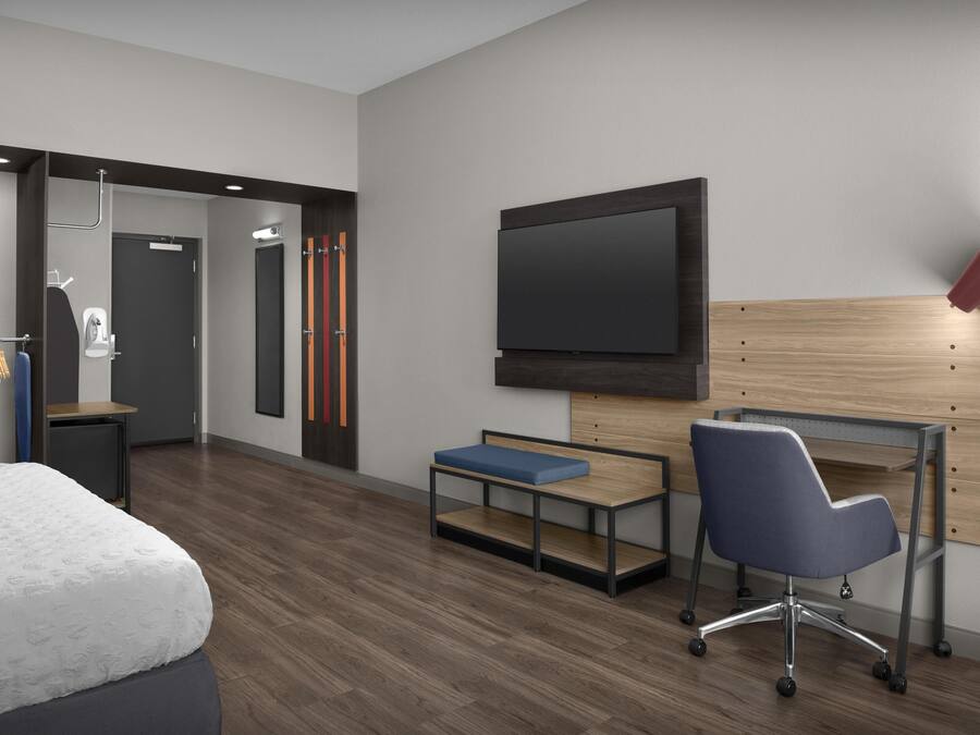 A modern hotel room with a bed, a desk with a chair, a TV mounted on the wall, and a shower area.