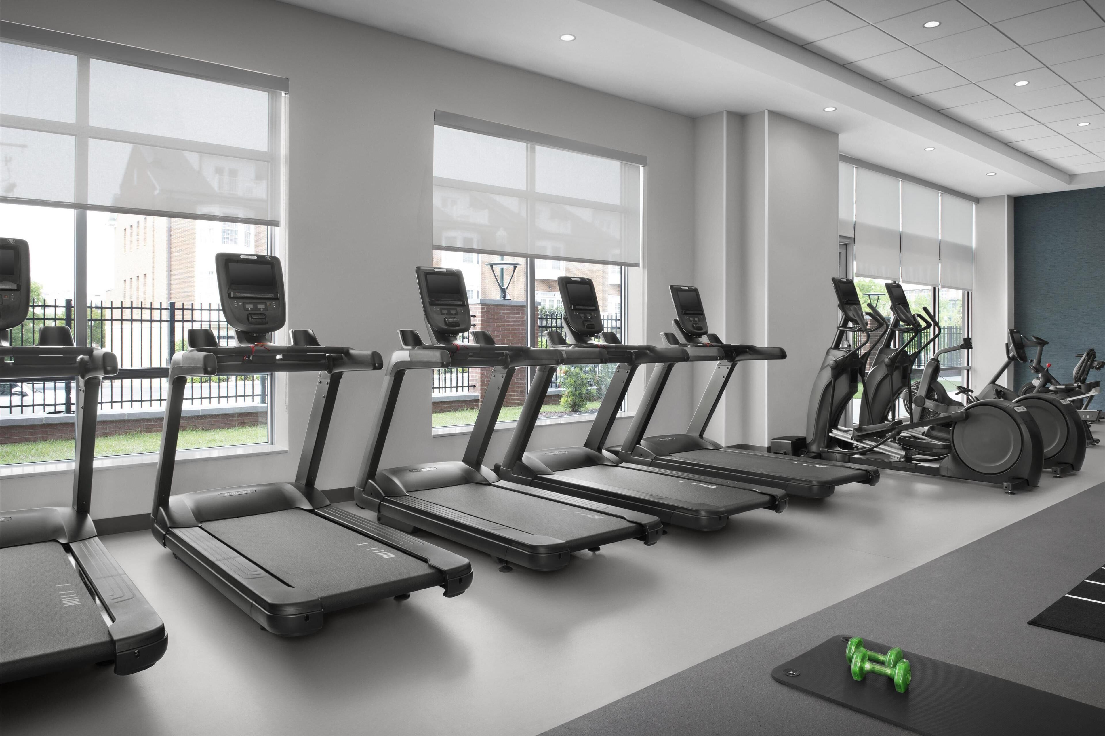 A gym with treadmills, a weight bench, and dumbbells.