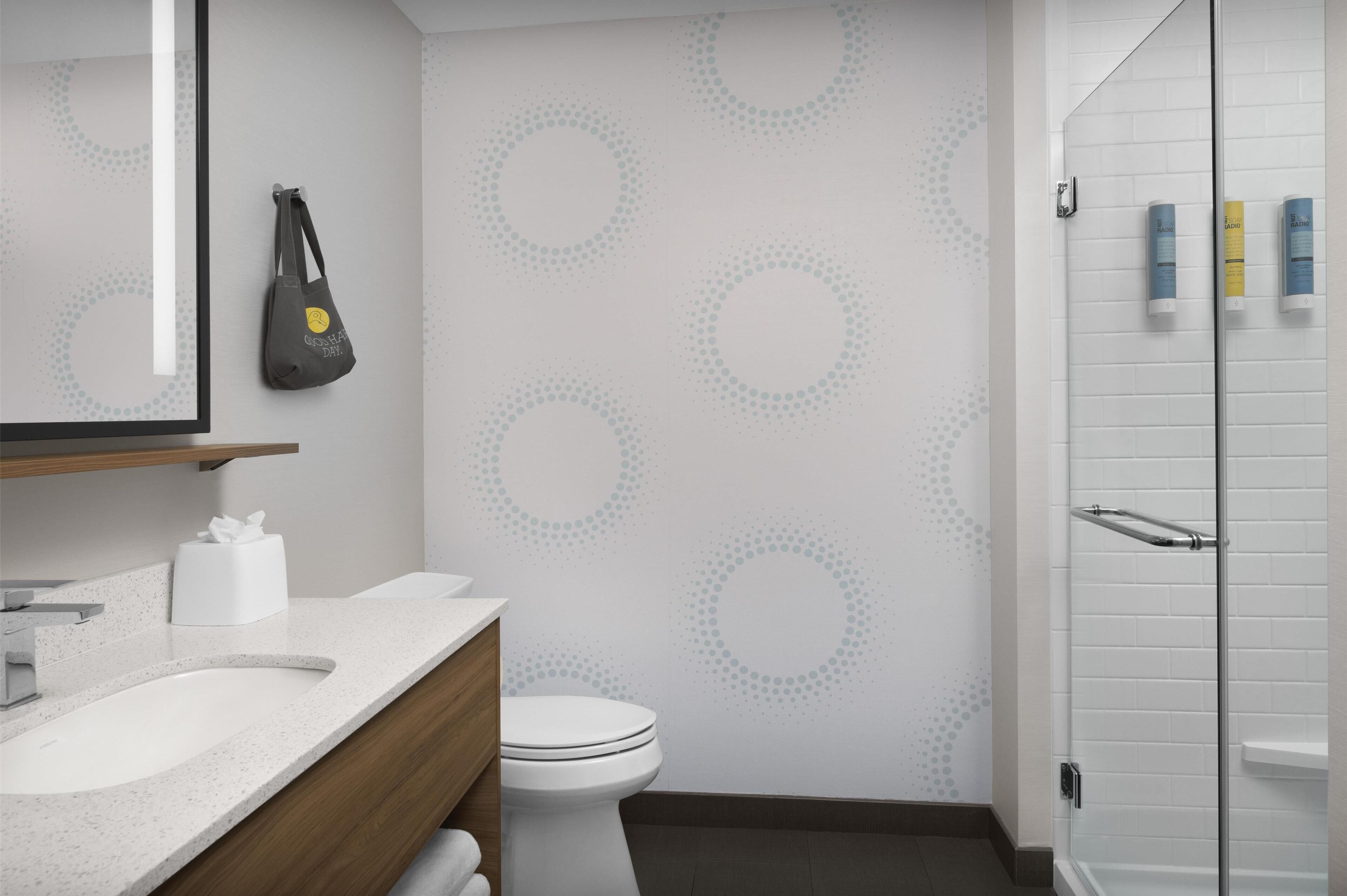 A modern bathroom with a white sink, toilet, and shower. There is a towel rack and a mirror above the sink.