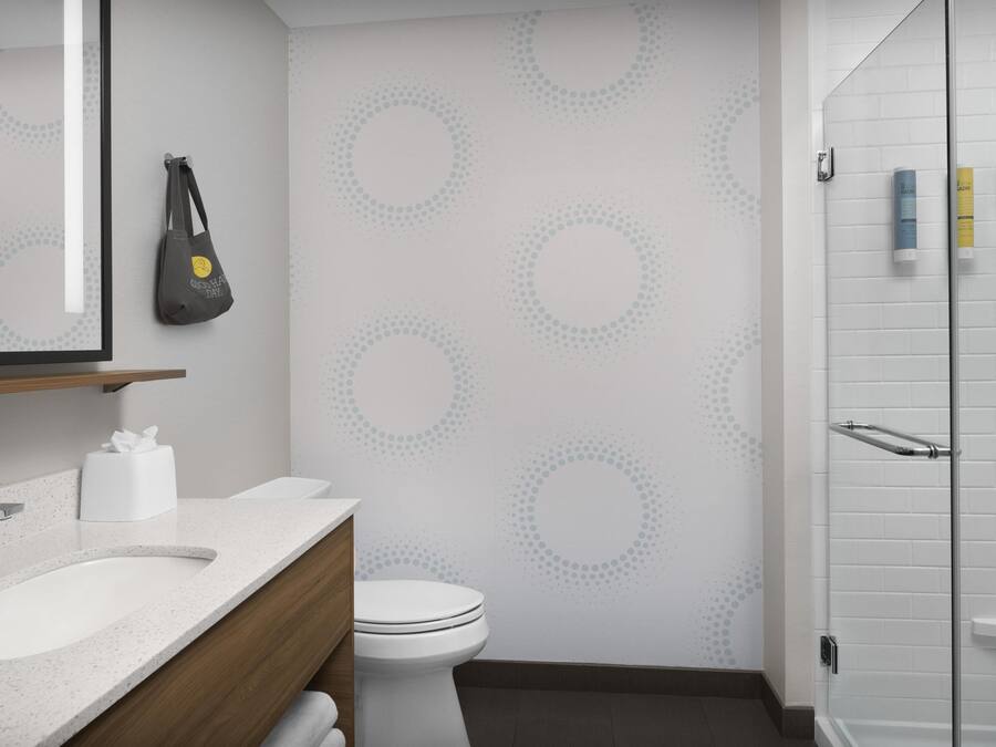 A modern bathroom with a white sink, toilet, and shower. There is a towel rack and a mirror above the sink.