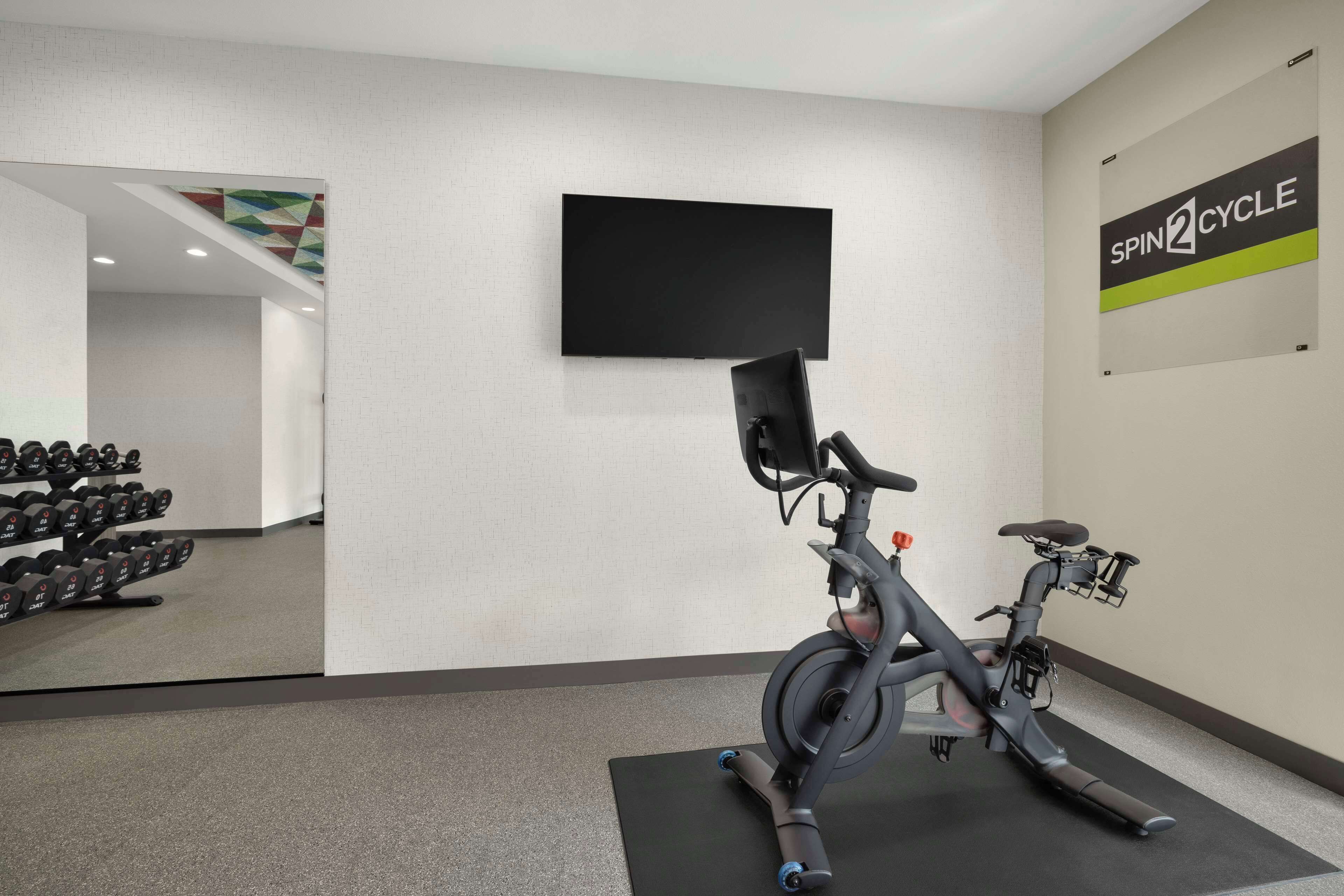 Un gimnasio con una bicicleta estática, un televisor y un letrero en la pared que dice "SPIN2CYCLE".
