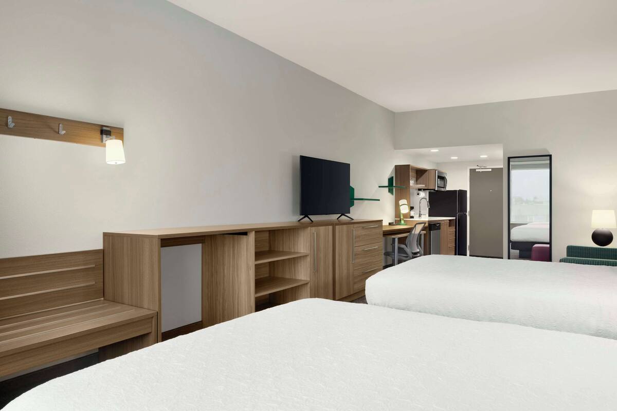 Ein Hotelzimmer mit zwei Betten, einem Schreibtisch, einem Flachbildfernseher, einer Mikrowelle und einer Küchenzeile.