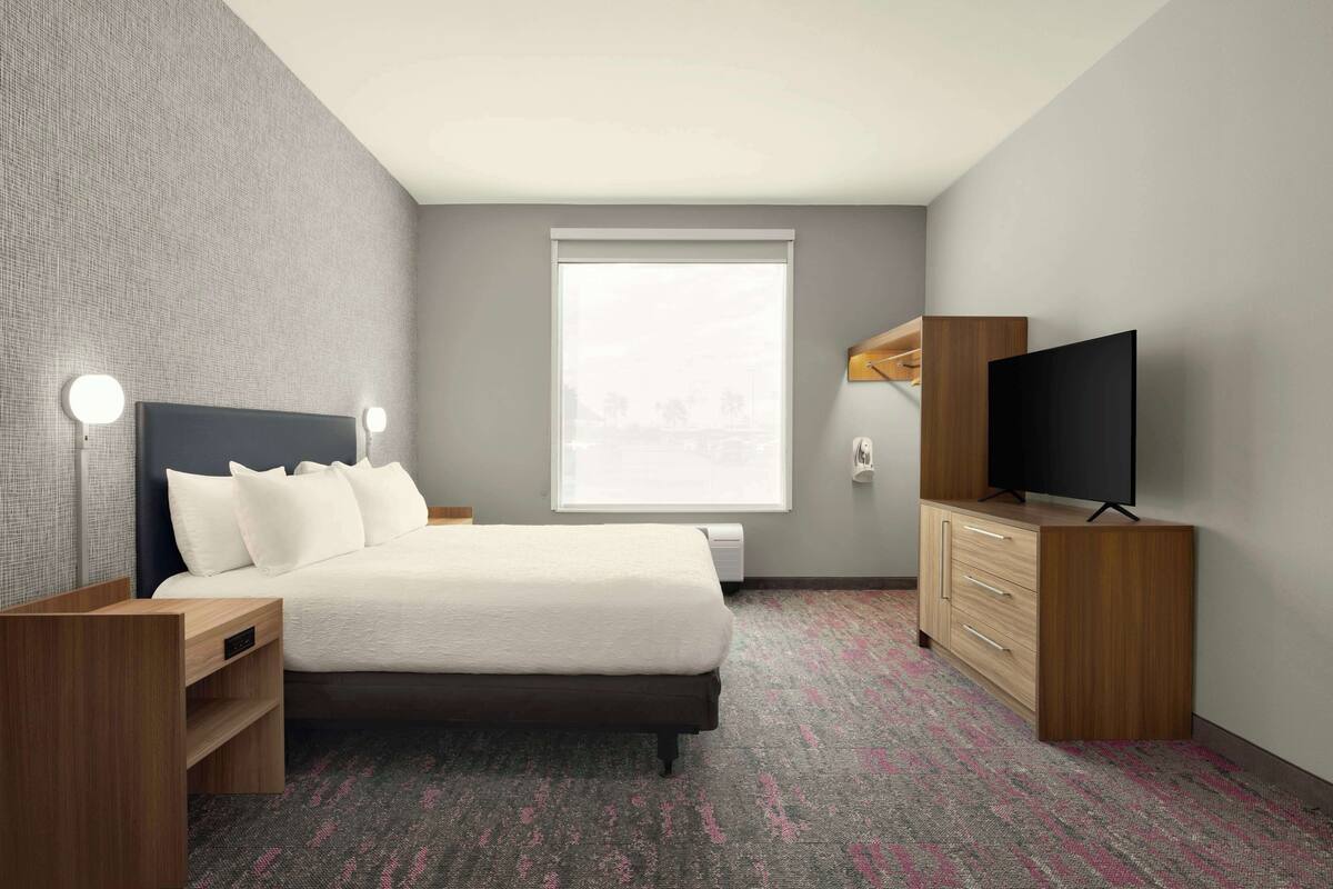 Ein Hotelzimmer mit Bett, Fernseher, Kommode und Fenster.