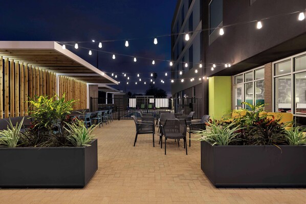 Un espace extérieur aménagé avec des tables et des chaises, entouré de jardinières remplies de plantes vertes.