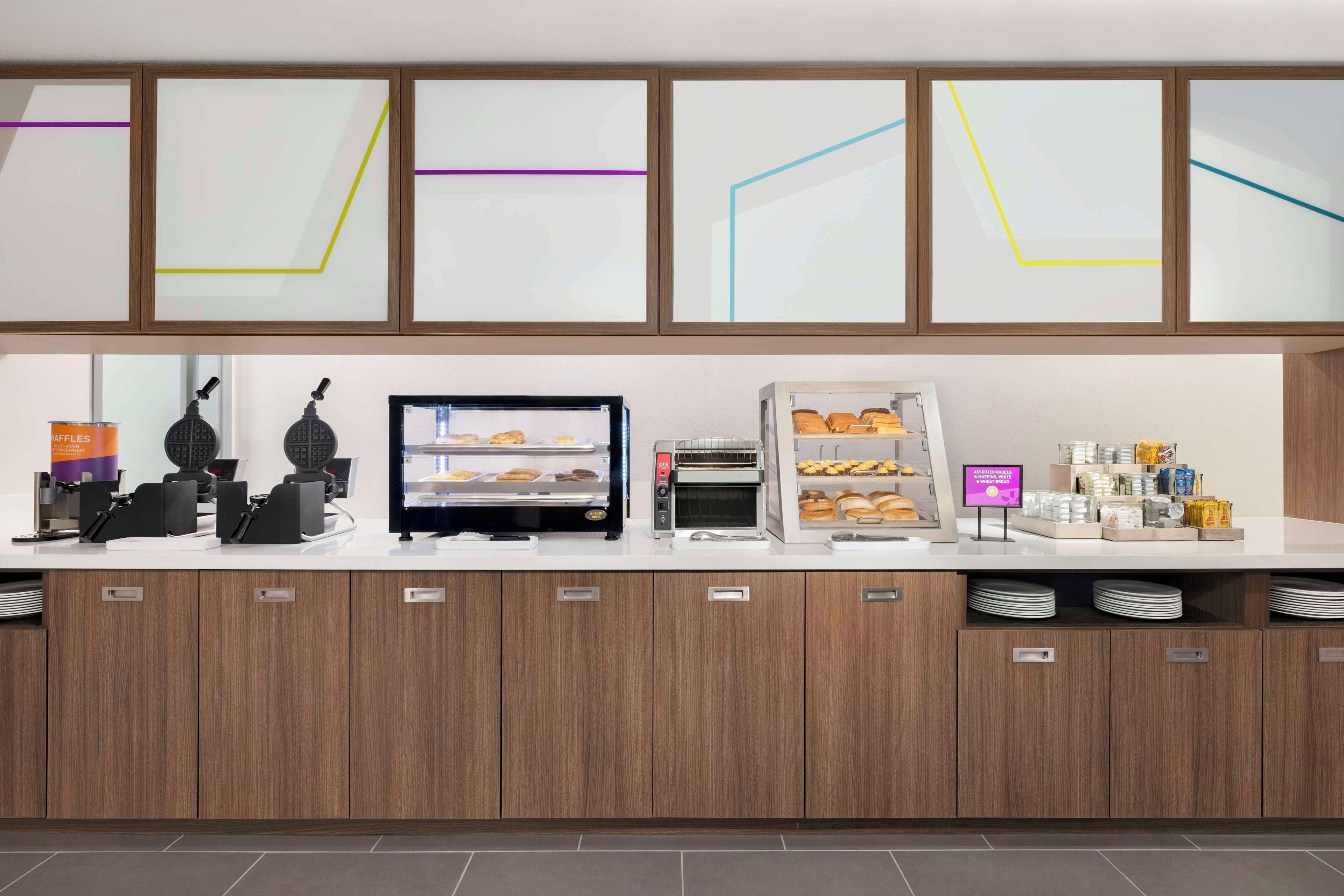 Um balcão de café da manhã moderno, com máquinas de waffle, uma vitrine e um canto para café.