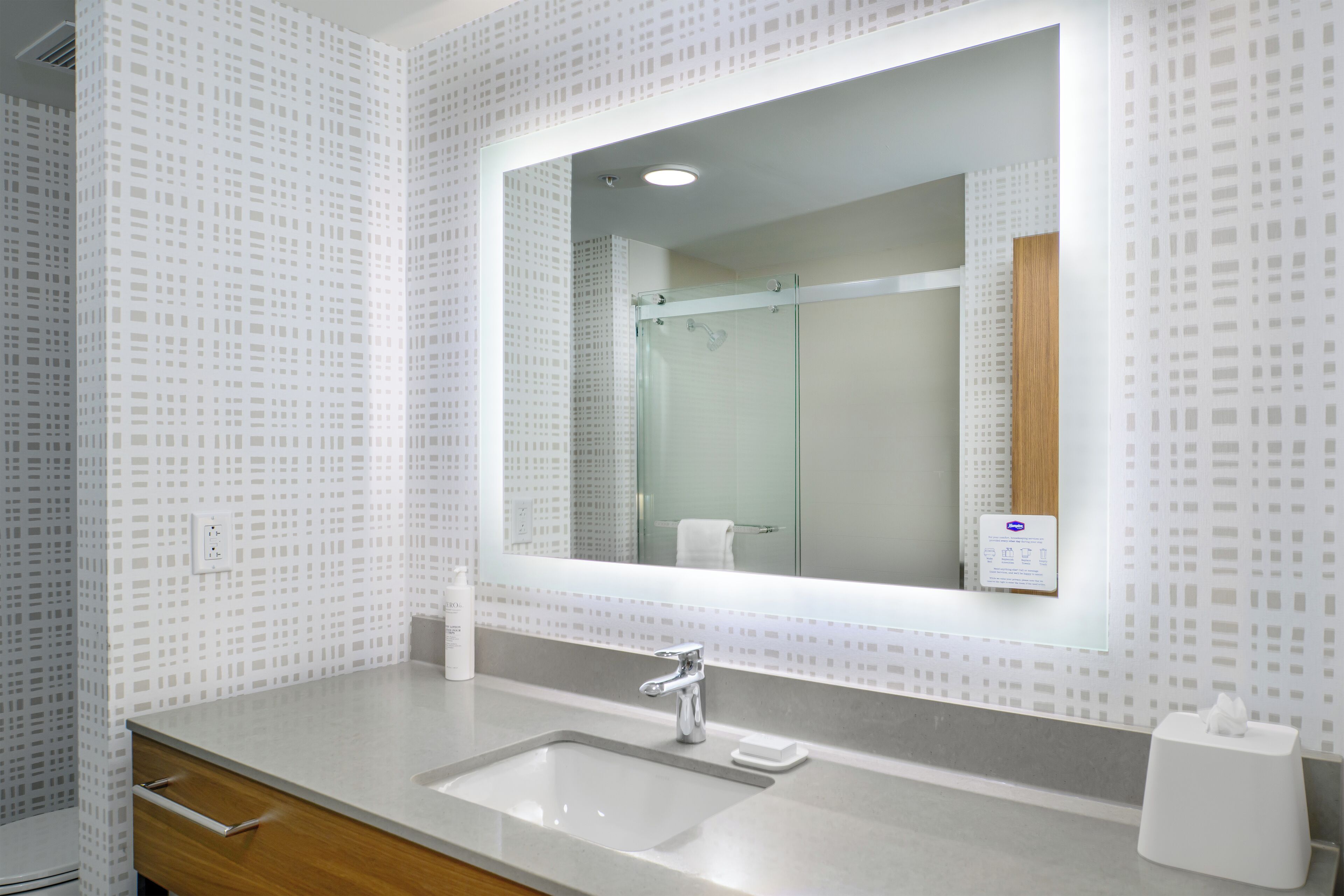 A modern bathroom with a large mirror, a sink, and a wooden vanity.