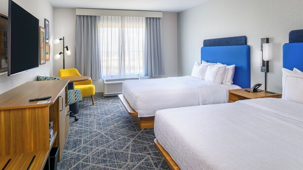 Une chambre d’hôtel avec deux lits, un bureau, une chaise, une télévision et une fenêtre avec des rideaux.