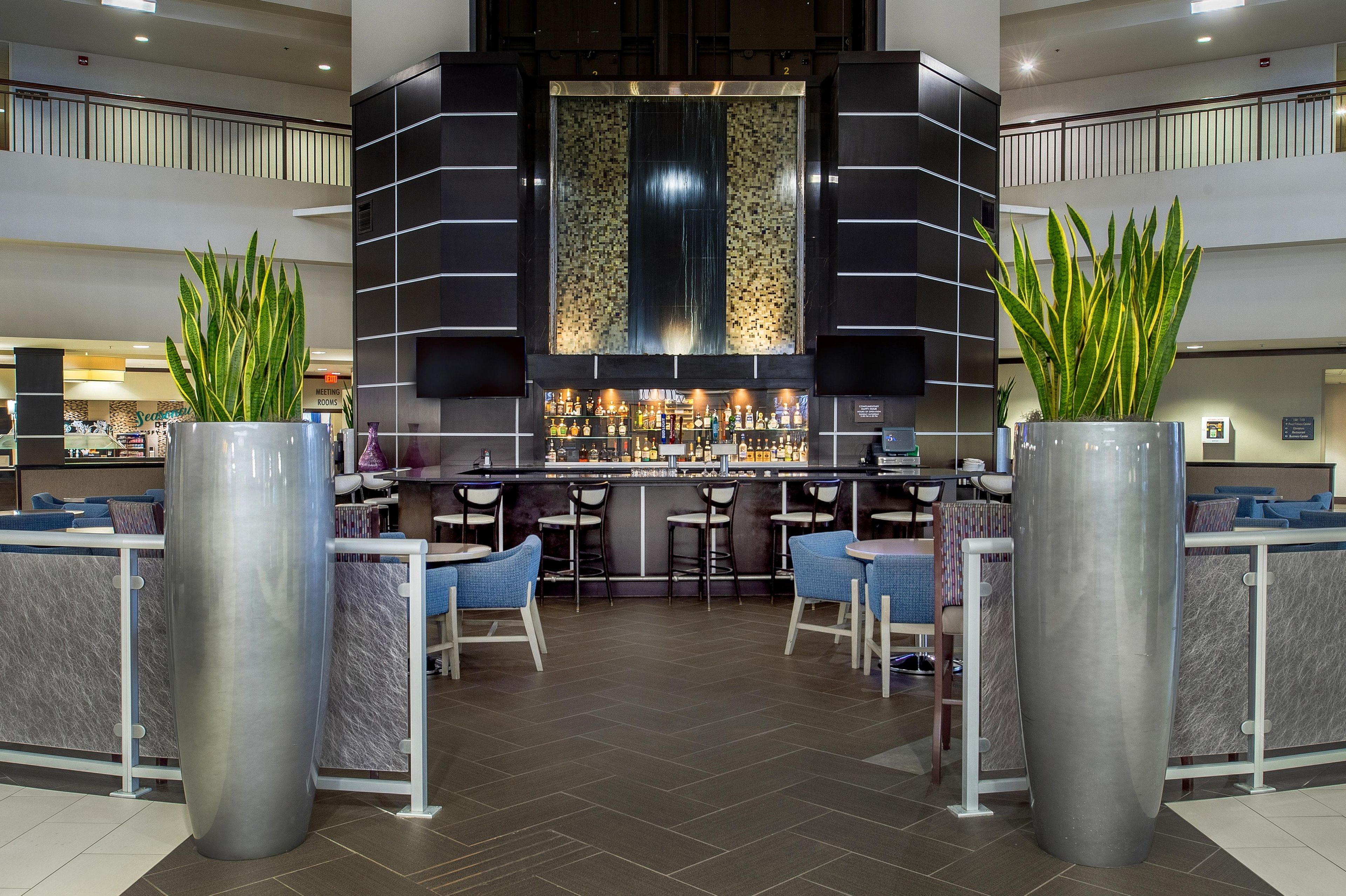 A modern bar area with a central bar counter, seating, and decorative plants.