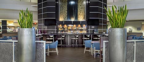 Zona de bar moderna con barra central, asientos y plantas decorativas.