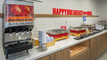 Morgenmadsbuffet med saftevandspumpe, et skilt med teksten "HAPPY BREAKFAST STARTS HERE." samt diverse madvarer og bestik.