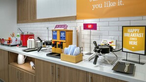 A breakfast station with coffee machines, waffle makers, and a sign indicating the start of breakfast. - Hampton Inn By Hilton St Louis Airport (St. Louis)