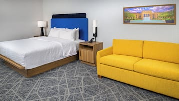 A hotel room with a bed, a nightstand, a lamp, a phone, a yellow sofa, and a painting on the wall.