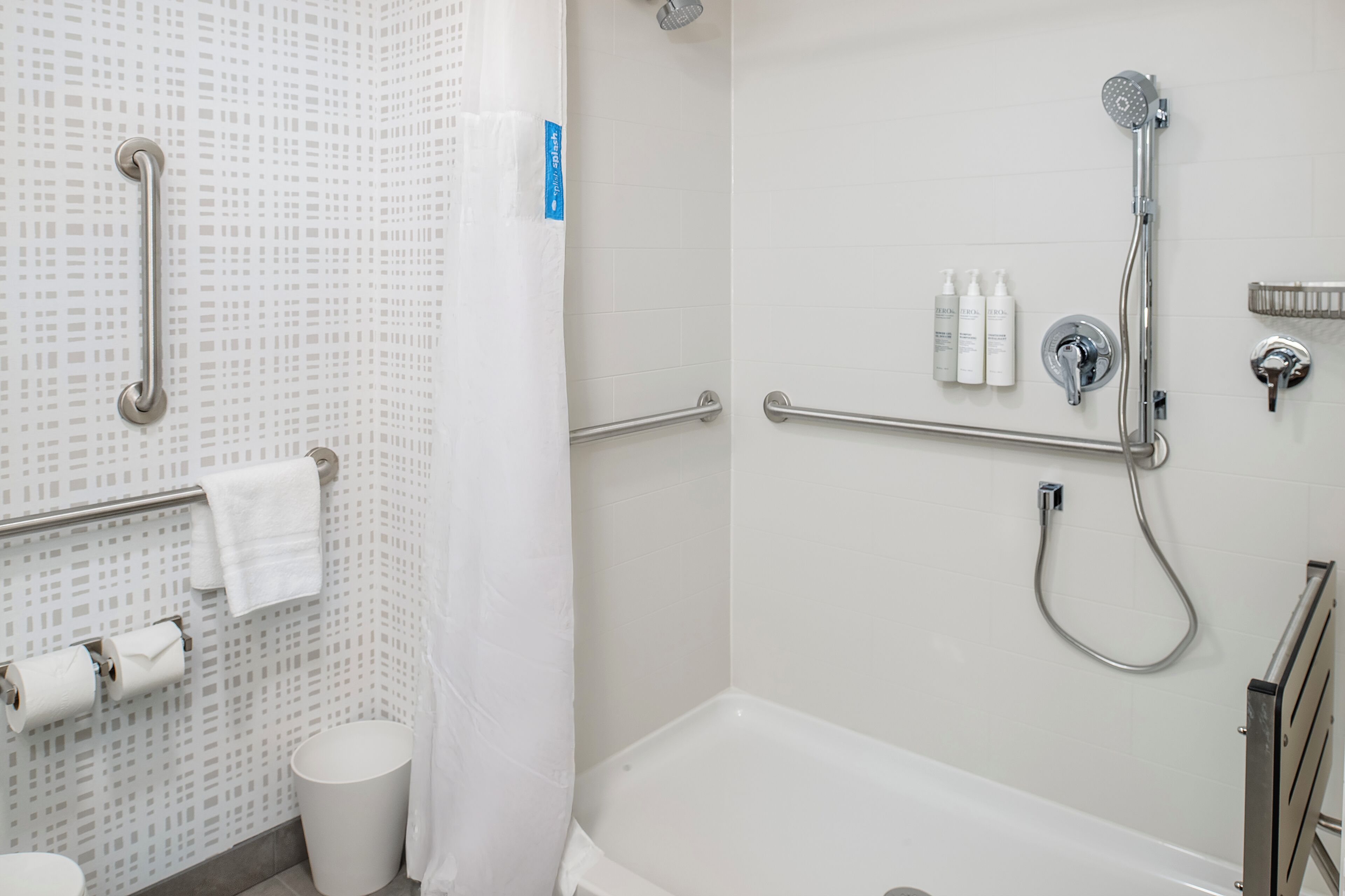 A bathroom with a shower, grab bars, a toilet, and a trash can.
