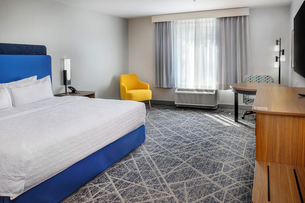 Habitación de hotel con una cama grande, un escritorio, una silla, un televisor y una ventana con cortinas.