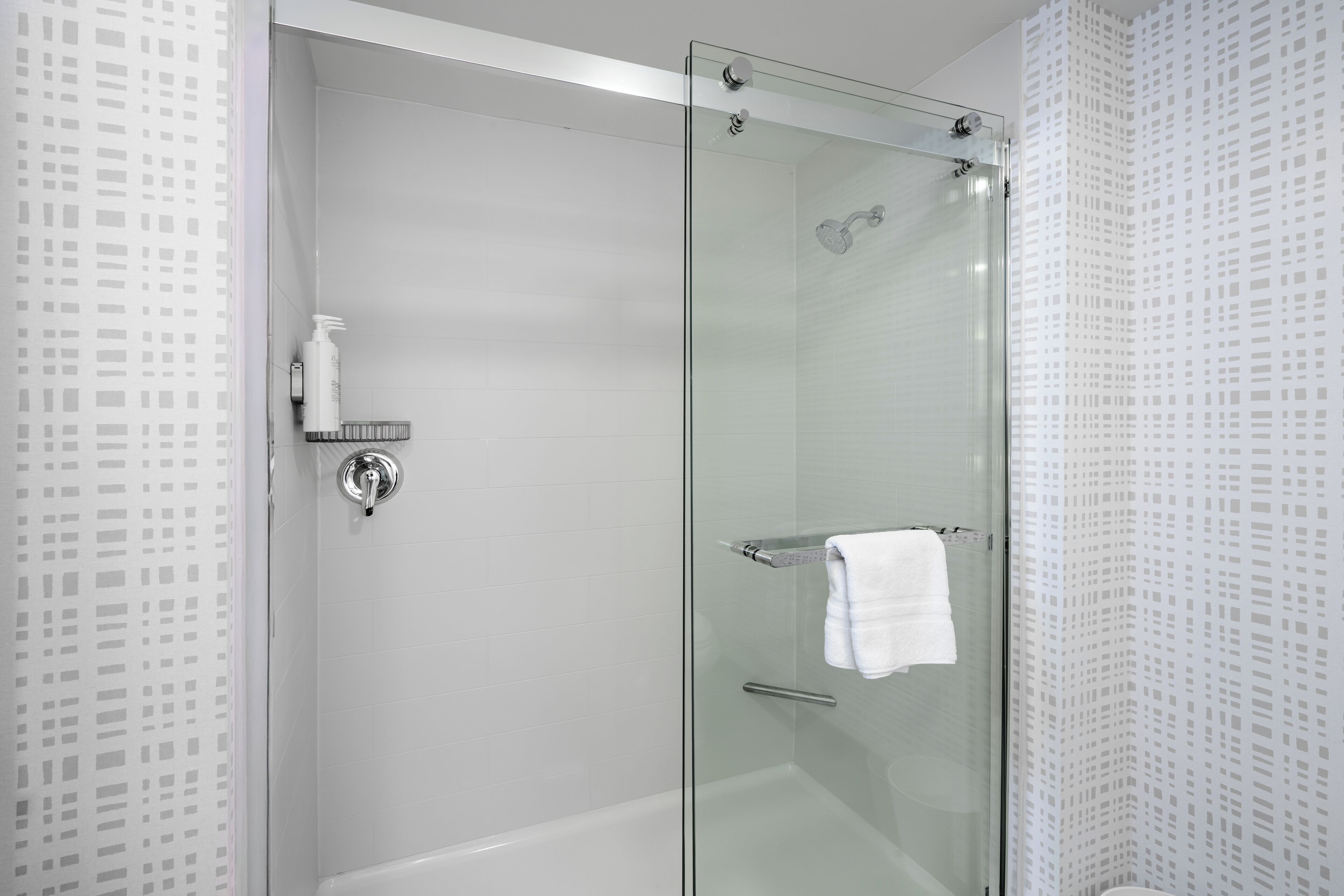 A modern bathroom with a glass-enclosed shower, a white tiled wall, and a glass door.