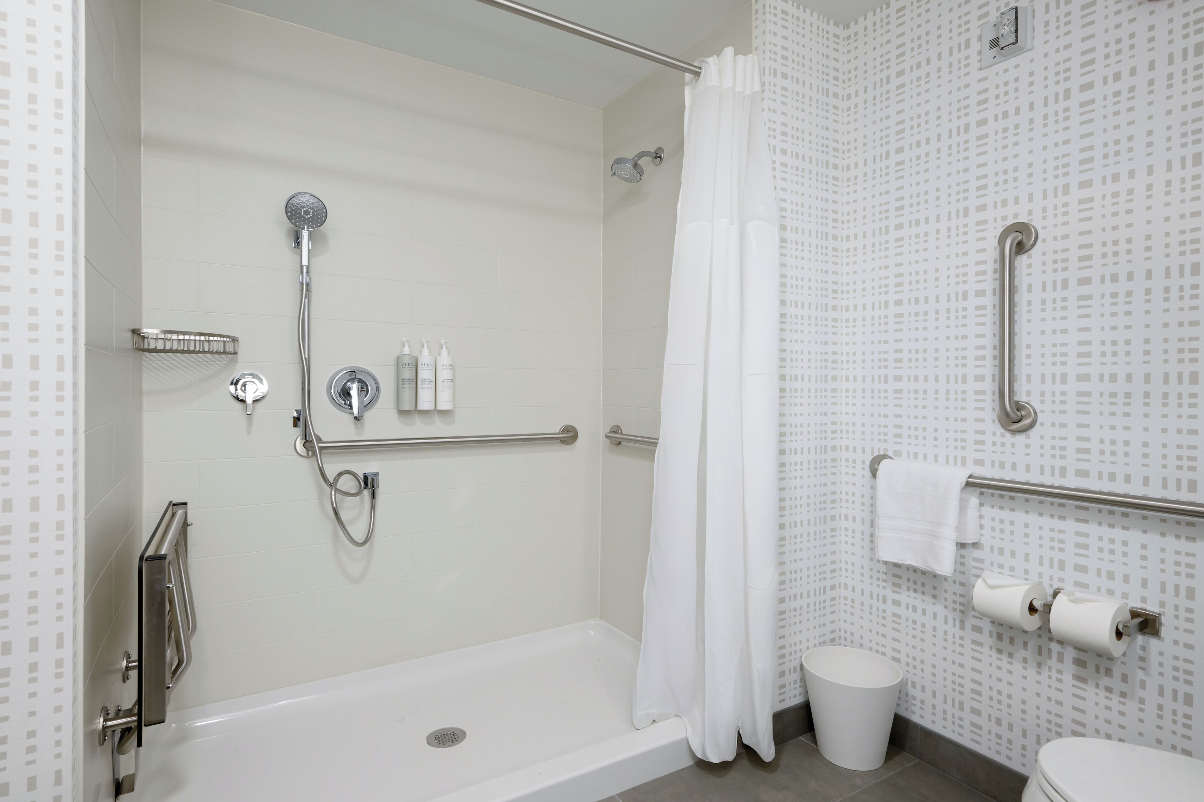Un baño moderno con cabina de ducha, barras de apoyo, inodoro blanco y cortina de ducha.