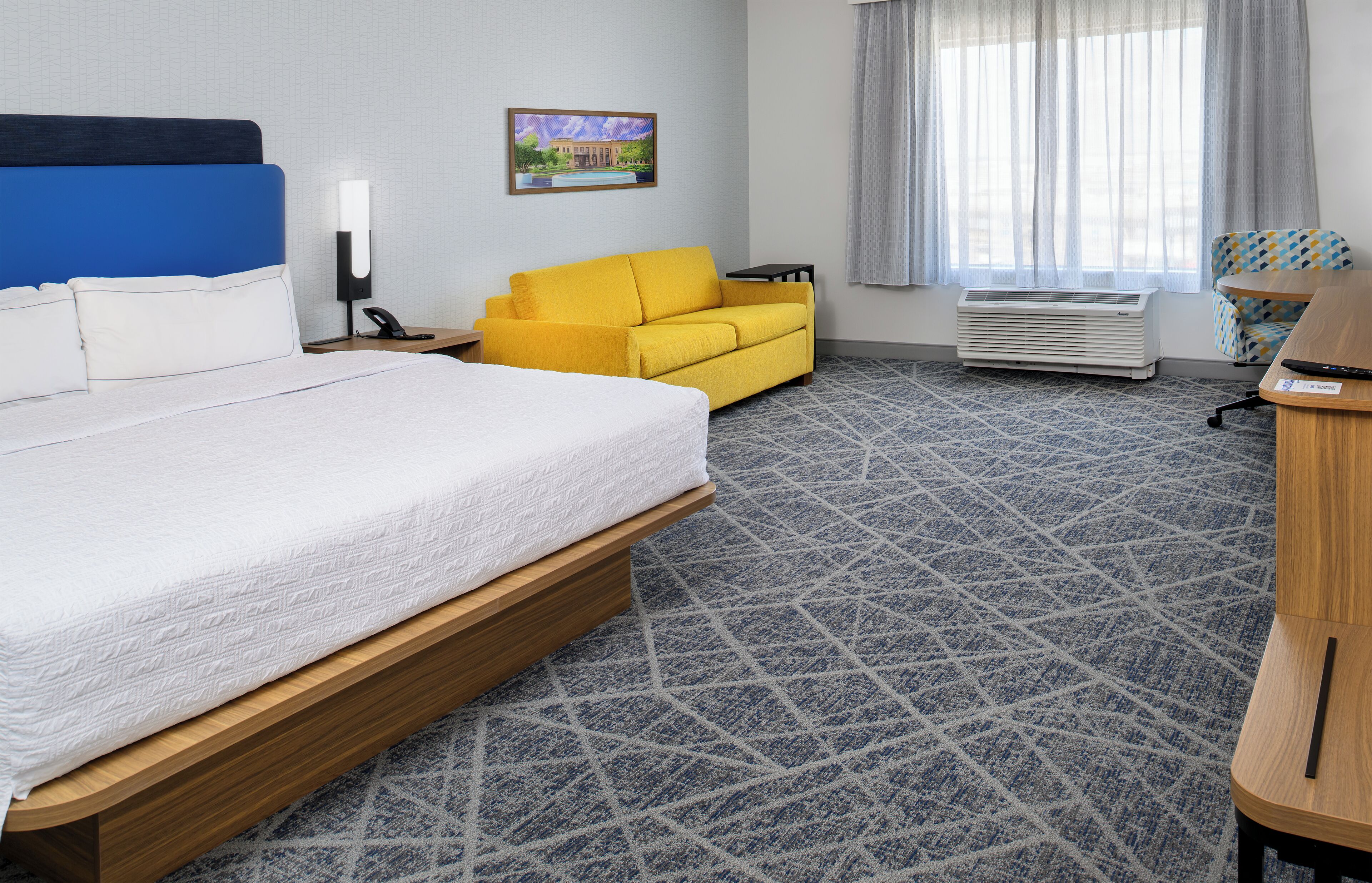 Una camera d'albergo con un letto grande, un divano giallo, una scrivania e una finestra con tende.