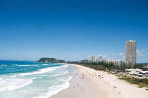 A beach with a long stretch of sand, ocean waves, and a tall building in the background. - Q1 Resort & Spa - Official (Surfers Paradise)