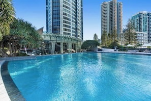A swimming pool surrounded by tall residential buildings, with a glass structure nearby. - Q1 Resort & Spa - Official (Surfers Paradise)