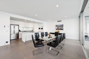 A modern kitchen with white cabinets, a stainless steel refrigerator, and a glass dining table with black chairs. - Q1 Resort & Spa - Official (Surfers Paradise)