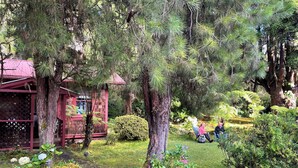 Una cabaña rústica con techo rojo, rodeada de densos pinos y un jardín bien cuidado.