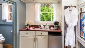 Cocina compacta con muebles blancos, cafetera y ventana con vistas a zonas verdes.