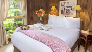 A neatly made bed with white and red linens, a vase of flowers, and a framed abstract painting on the wall. - Private Cottage at Boutique Hotel in Volcano Village (Volcano)