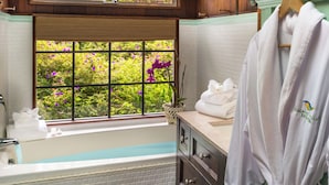 A bathroom with a bathtub, a window with a view of greenery, and a towel rack with a robe. - Private Cottage at Boutique Hotel in Volcano Village (Volcano)