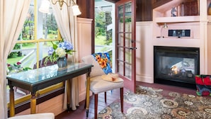 A cozy room with a fireplace, a glass table, and a chair with a floral blanket. - Private Cottage at Boutique Hotel in Volcano Village (Volcano)