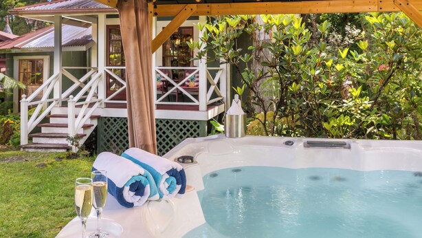 A hot tub with towels and champagne glasses, surrounded by lush greenery and a wooden deck. - Private Cottage at Boutique Hotel in Volcano Village (Volcano)