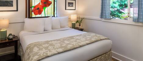 A neatly made bed with a floral bedspread, a nightstand with a lamp, and a window with curtains.