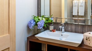 Ein Badezimmer mit einem Holzwaschtisch, einem weißen Waschbecken, einem Spiegel und einer Vase mit Blumen.