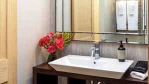 Een badkamer met een witte wasbak, een spiegel, een vaas met rode bloemen en een handdoekrek met witte handdoeken.